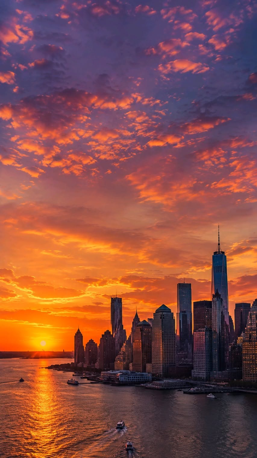 Dramatic City Skyline with Fiery Sunset Reflection Over Water